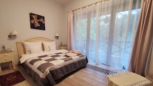 Une chambre avec un lit en bois, une table de chevet, une commode, une fenêtre avec des rideaux légers et une vue sur les arbres.