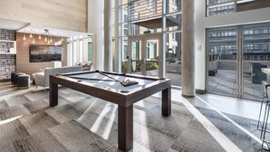 Ein moderner Poolbereich im Innenbereich mit Billardtisch, Sitzgelegenheiten und großen Fenstern mit Blick auf die Stadt.