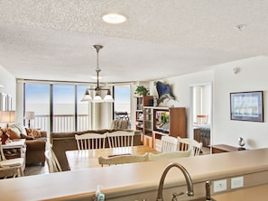 Relax in this inviting living area with a large dining table and kitchenette, featuring a high ceiling and expansive window with a view.