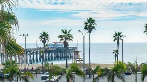 Un muelle que se adentra en el agua, con palmeras y una playa al frente.