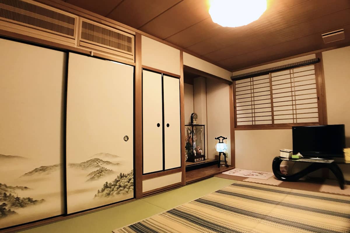 A traditional Japanese room with tatami flooring, sliding doors, a television on a stand, and a decorative lamp.