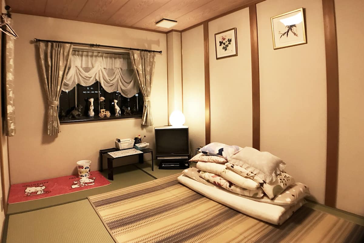 A room with a bed, a TV, a small table, and a window with curtains.