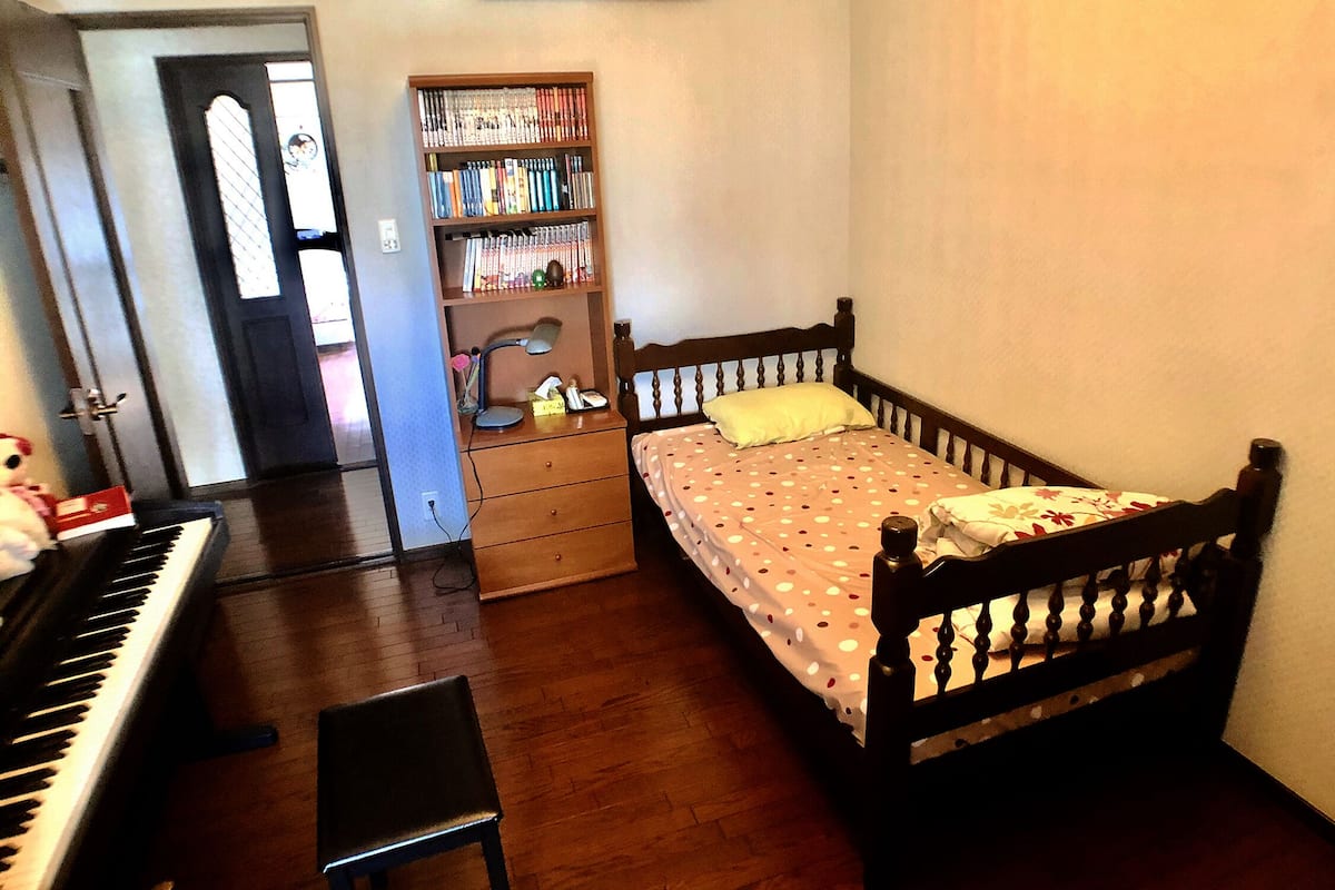 A bedroom with a bed, a wooden headboard, a nightstand, a bookshelf, a desk with a keyboard, and a chair.