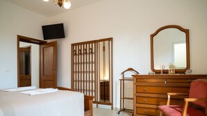Un dormitorio con cama, cómoda, silla, espejo y televisor en la pared.