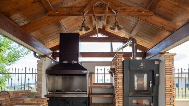 Una cocina rústica al aire libre con chimenea, horno empotrado y pileta.