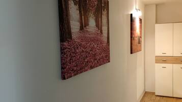 A hallway with a large painting of a forest scene on the wall, a light fixture, and a wooden cabinet.