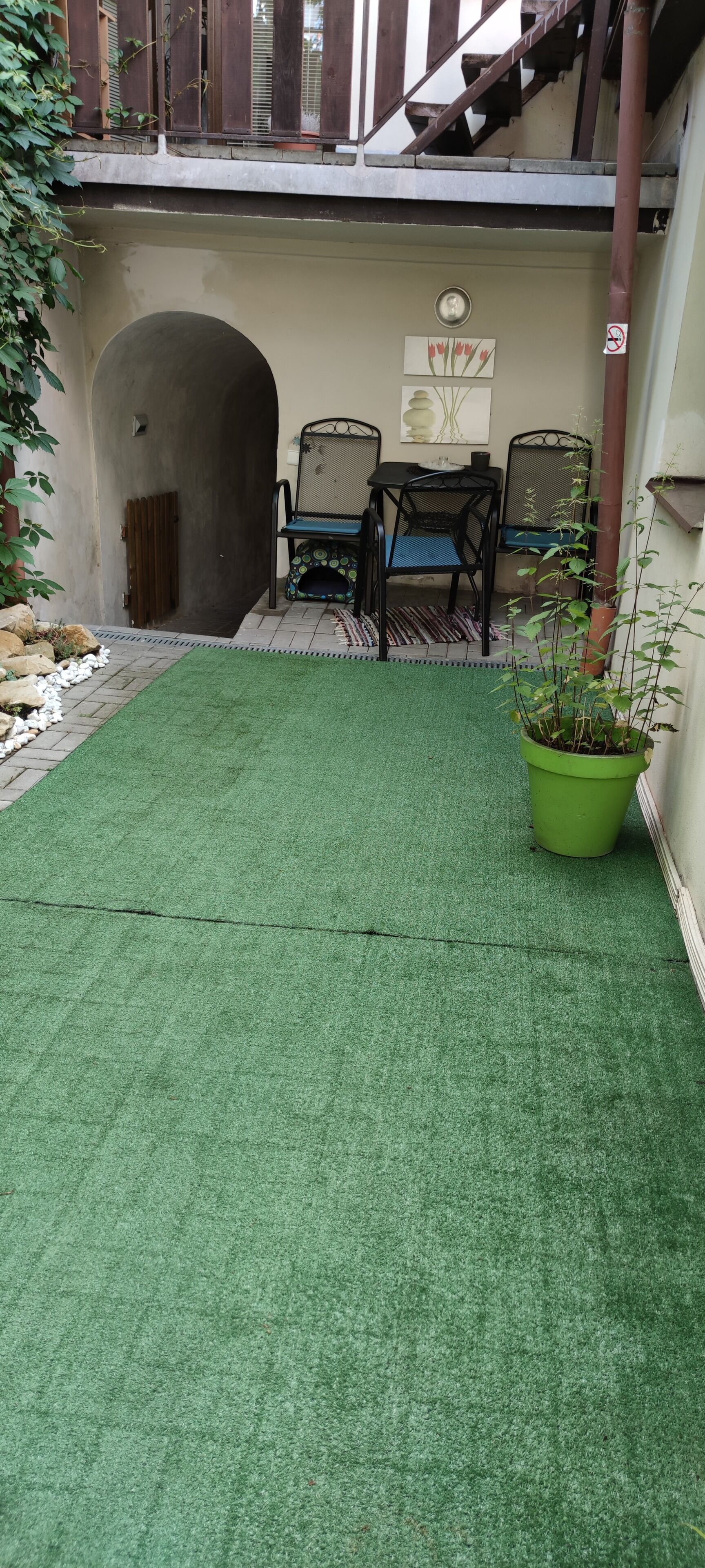 Un espace patio avec une pelouse artificielle, une plante verte en pot et un coin salon composé de chaises et d’une table.