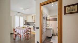 Een kleine keuken met moderne apparaten, een eethoek met een tafel en stoelen, en een gang die naar een badkamer leidt.