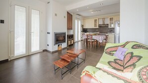 Een ruime woonkamer met een bank, houten bankjes, een televisie en een keuken op de achtergrond.