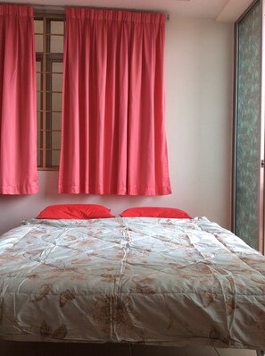 Cozy bedroom with a bed and floral-patterned bedspread, featuring a window with curtains and a door.