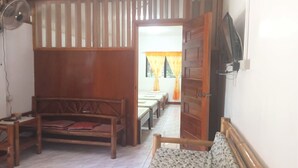 Een kamer met een houten bed, een bank, een aan de muur bevestigde televisie en een raam met gordijnen.