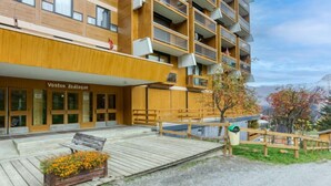 Ein modernes Gebäude mit Holzfassade, einer Holzterrasse mit Bank und Blumenbeet sowie einem Schild mit der Aufschrift 'Vostok Zodiac'.