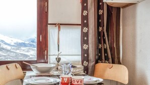 Ein Esszimmer mit Tisch, Tellern, Schüsseln und Tasse, mit Blick auf verschneite Berge durch ein Fenster.