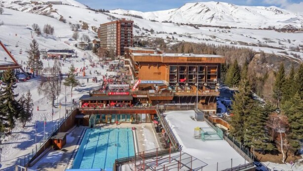 Ein Skigebiet mit Poolbereich, einem Gebäude mit mehreren Balkonen und einem Berg im Hintergrund.