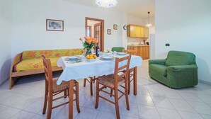 Uma área de refeições com uma mesa posta para quatro pessoas, um sofá verde e uma poltrona verde.