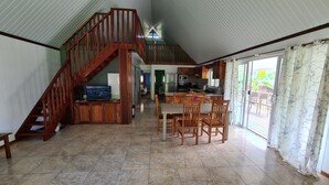 A spacious living area with a wooden staircase, a kitchen, and a dining area. - FARE AT MARIE LOU (Papetoai Moorea)