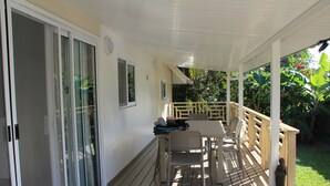 A covered outdoor patio with a table and chairs, a small statue, and a view of lush greenery. - FARE AT MARIE LOU (Papetoai Moorea)