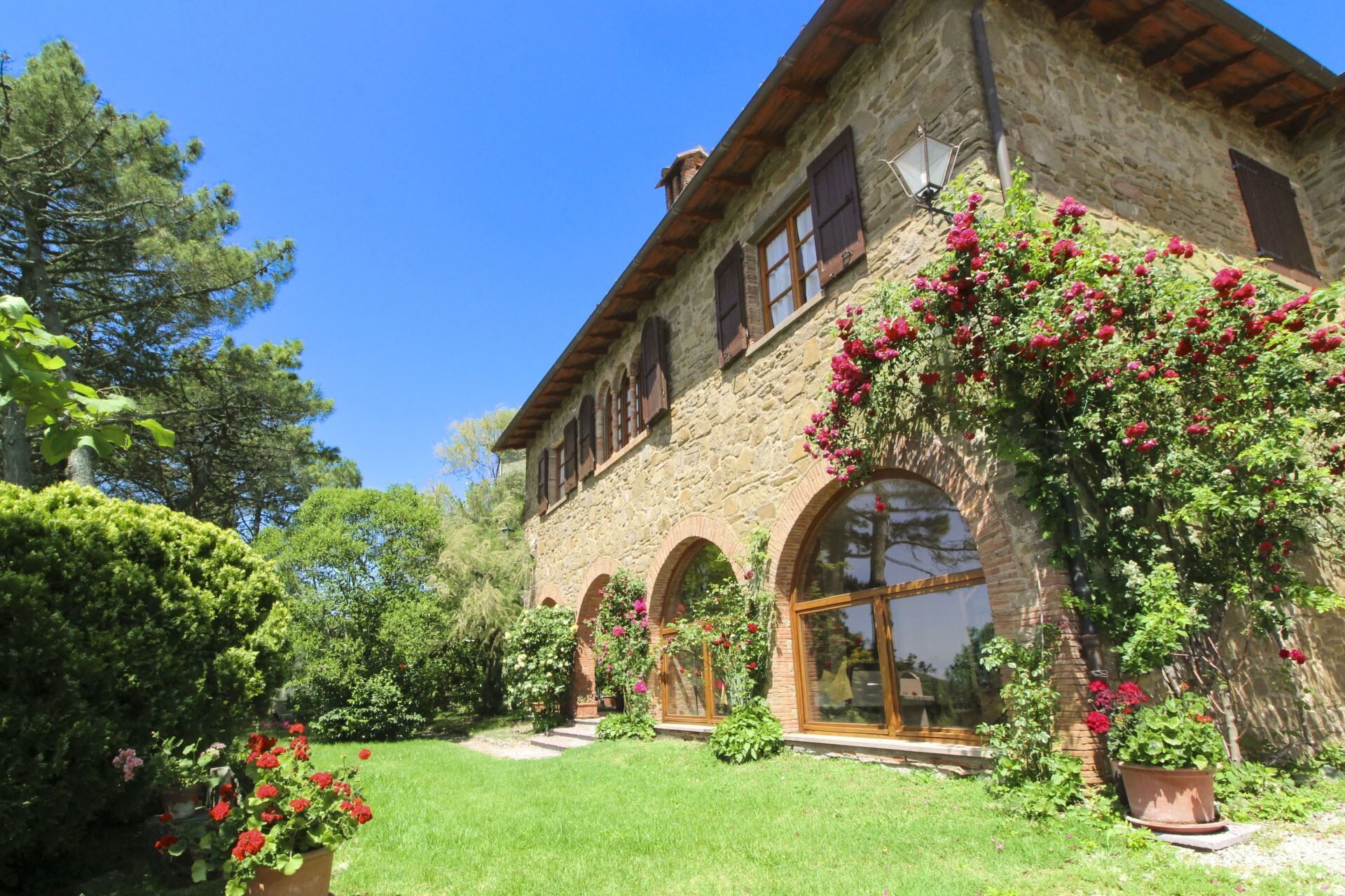 A stone building with arched windows and a garden with flowering plants.