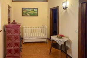 Una habitación con una cuna blanca, un armario rojo, una mesa con mantel de encaje y un cuadro en la pared.