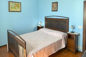 Un dormitorio con cama, mesita de noche, lámpara y dos cuadros en la pared.