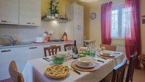 A dining area with a table set for a meal, chairs, a kitchen in the background, and a window with curtains. - Beautiful  villa for 4 people with WIFI, TV and terrace (Massa)