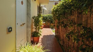 A narrow pathway leading to a building with a white door, potted plants, and a bamboo fence. - Beautiful  villa for 4 people with WIFI, TV and terrace (Massa)