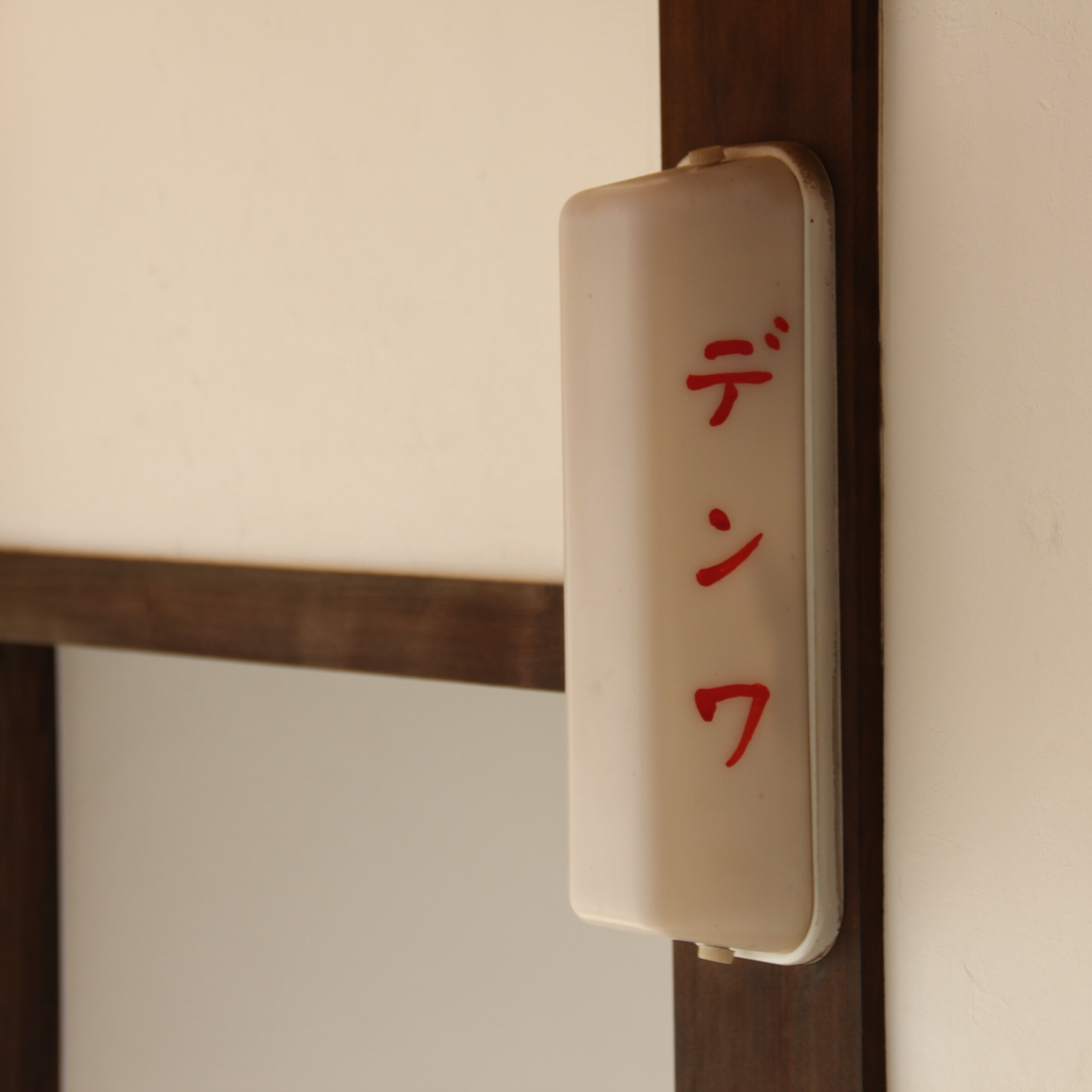 A white sign with red Japanese characters on a wooden door frame.