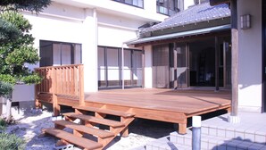Une terrasse en bois dotée de bancs intégrés, un patio couvert et une vue sur un bâtiment aux grandes fenêtres.