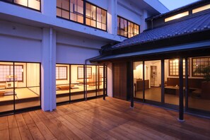 Un edificio de varios pisos con terraza de madera y puertas correderas de vidrio que dan a un interior tradicional.