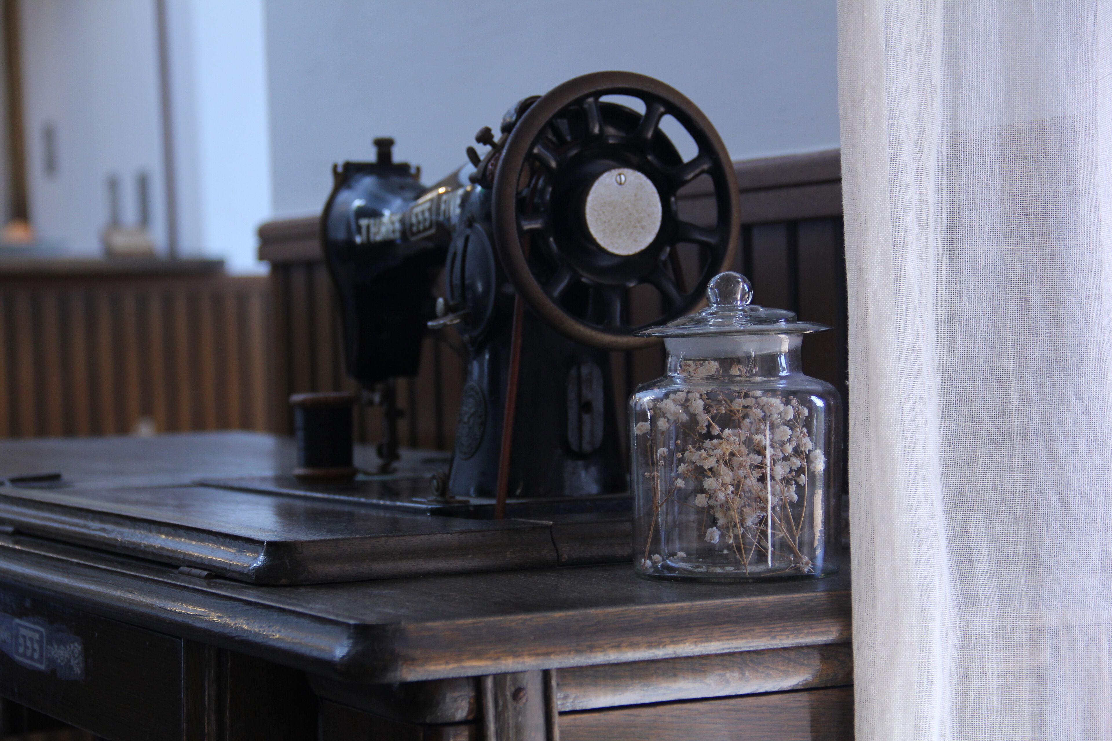 A vintage sewing machine and a glass jar with dried flowers on a wooden table.