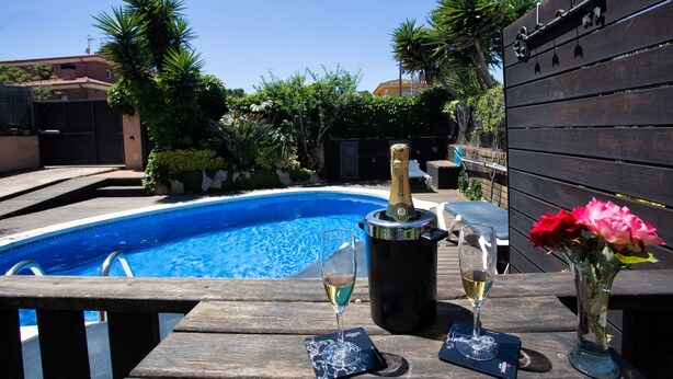 A poolside setting with a wooden deck, a pool, and a bottle of champagne.