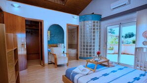 A bedroom with a bed, a wooden wardrobe, a bathroom with a shower, and a balcony with a view.
