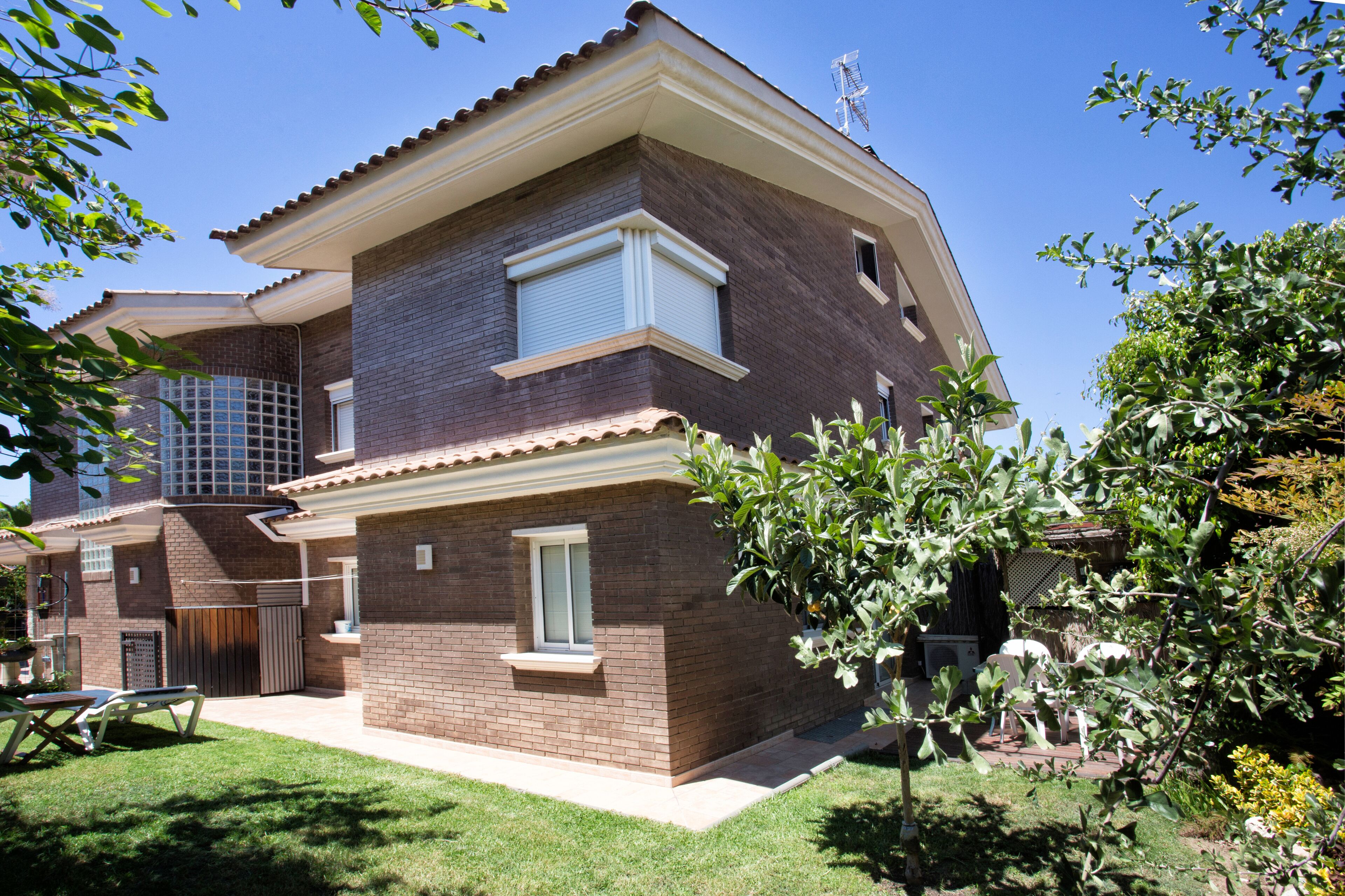 A two-story house with a brick exterior, a covered patio, and a small garden area.
