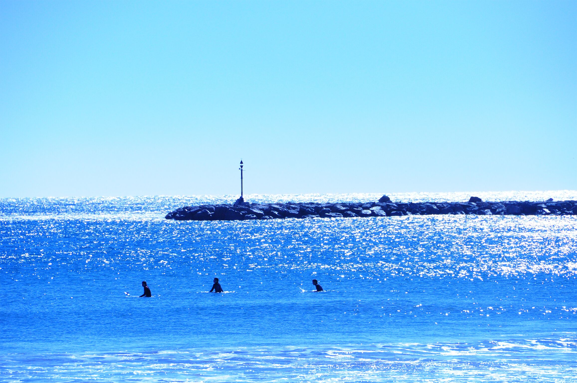 Un muelle se adentra en un mar azul cristalino con un faro al final.