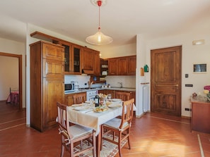Une cuisine avec des meubles de rangement en bois, une table à manger pour quatre personnes et un luminaire suspendu.