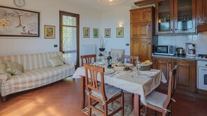 Una sala de estar acogedora con sofá, mesa de comedor y sillas, una cocina con armarios de madera y electrodomésticos, y obras de arte en las paredes.