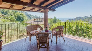 Un balcón con mobiliario de mimbre, una mesa con una botella y vistas a un paisaje montañoso.