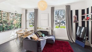Un salon moderne avec un canapé gris, un tapis rouge et une grande fenêtre avec des rideaux.