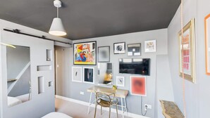 Une chambre moderne avec un lit, un bureau et une chaise. Plusieurs tableaux encadrés ornent le mur.