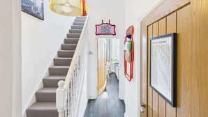 Un escalier avec une rampe, un luminaire suspendu, une porte avec une plaque, et un objet fixé au mur.
