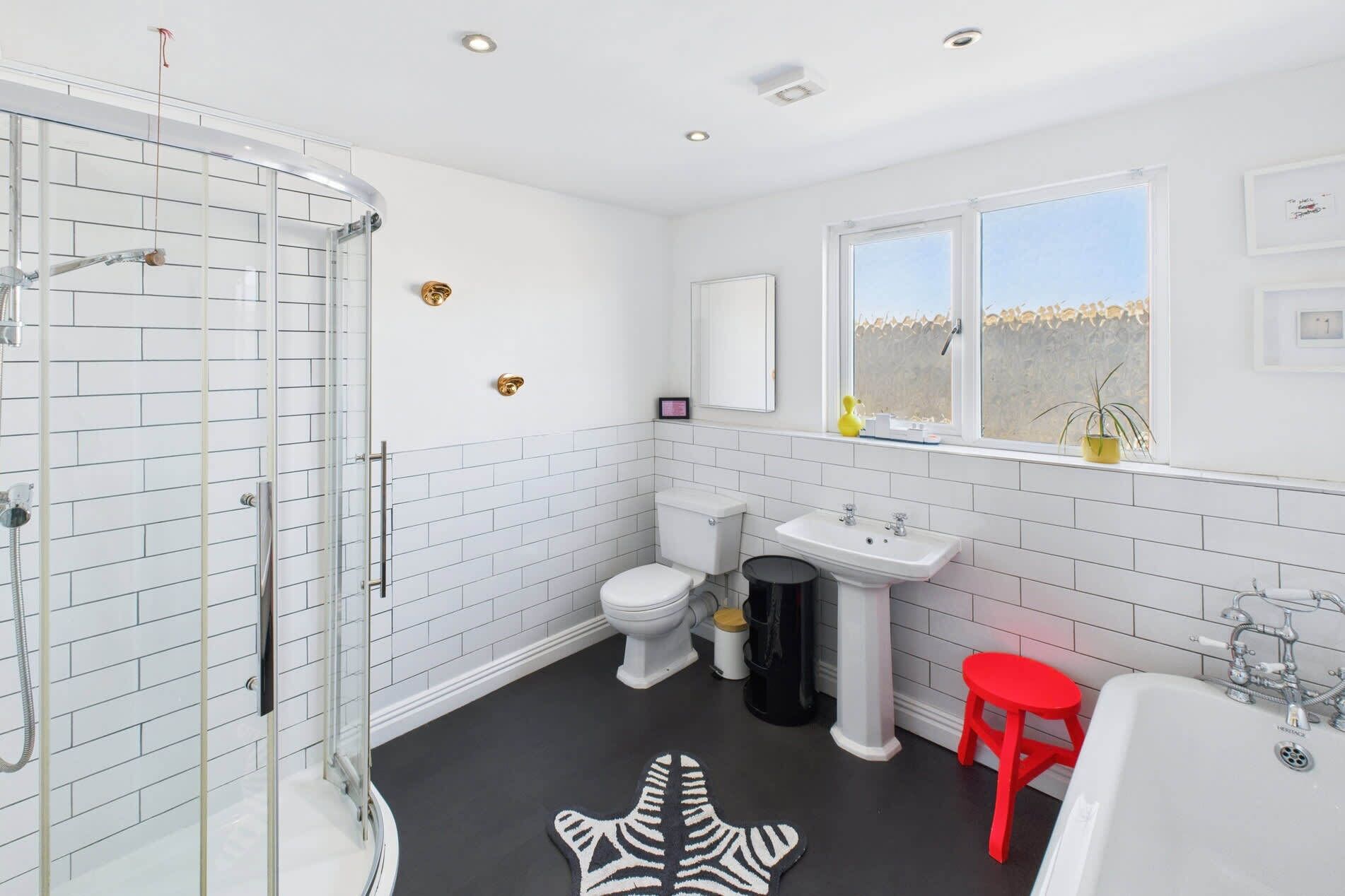 Et moderne badeværelse med et glasbadeværelsesafskærmning, et hvidt toilet, et konsolbord og en rød skammel.