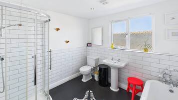 Et moderne badeværelse med et glasbadeværelsesafskærmning, et hvidt toilet, et konsolbord og en rød skammel.