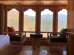 Een houten kamer met een bed, twee stoelen, een tafeltje en grote ramen met uitzicht op de bergen.