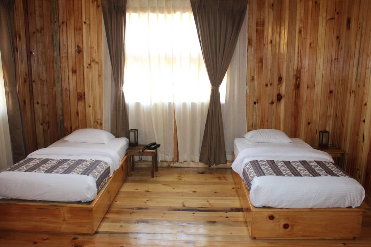 A room with two wooden beds, a small table, and a telephone.