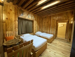A wooden cabin room with two beds, a wooden chair, a window with curtains, and a door. - Haa Heritage Hotel (Ha)