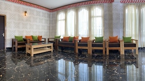 Un vestíbulo con piso de mármol, sofás de madera con cojines verdes y naranjas, y papel tapiz estampado.