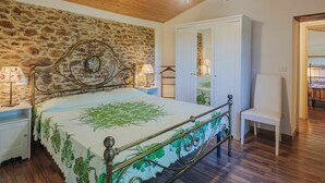 Une chambre avec un mur en pierre, un lit avec un cadre en métal, une armoire blanche et un plafond en bois.