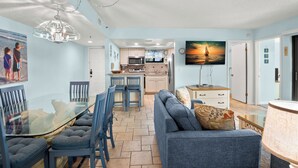 Une cuisine moderne avec un îlot central, un coin repas doté d’une table en verre et un salon avec un canapé et une lampe.
