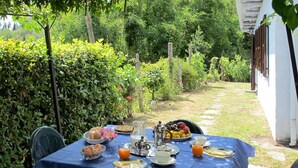 Un tavolo all'aperto apparecchiato per la colazione, con uova, pane tostato, frutta e bevande, in un giardino.