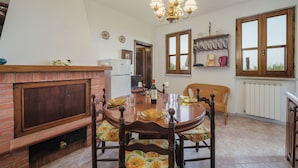 Zona pranzo con camino in mattoni, un lampadario e vista all'esterno attraverso ampie finestre.